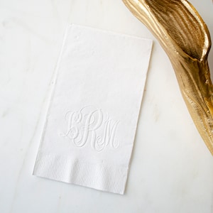 May include: White linen napkin with a raised, embossed monogram of the letters "SRM" in a script font.