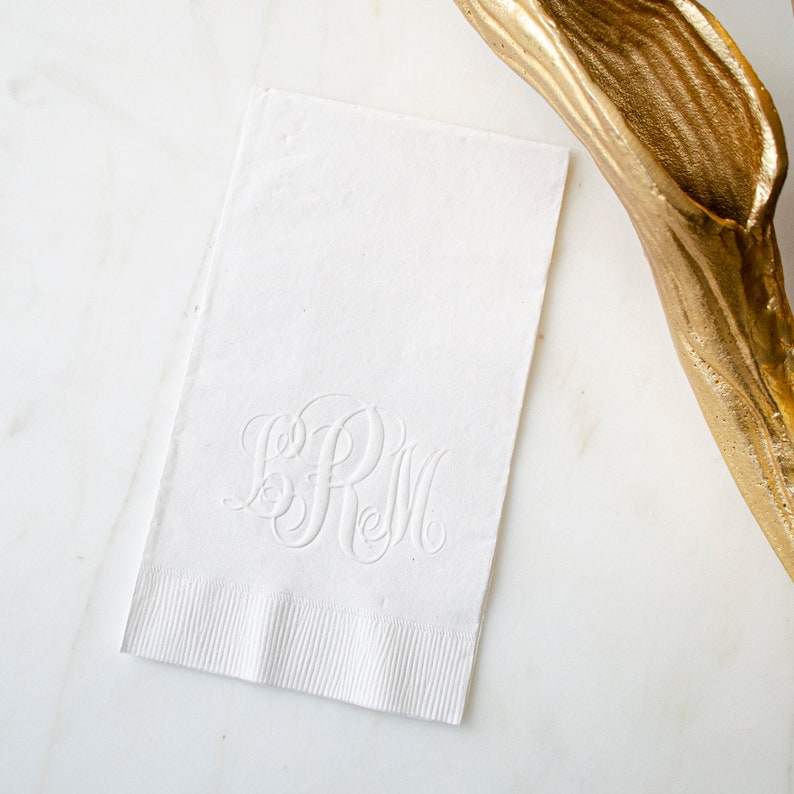 May include: White linen napkin with a raised, embossed monogram of the letters "SRM" in a script font.
