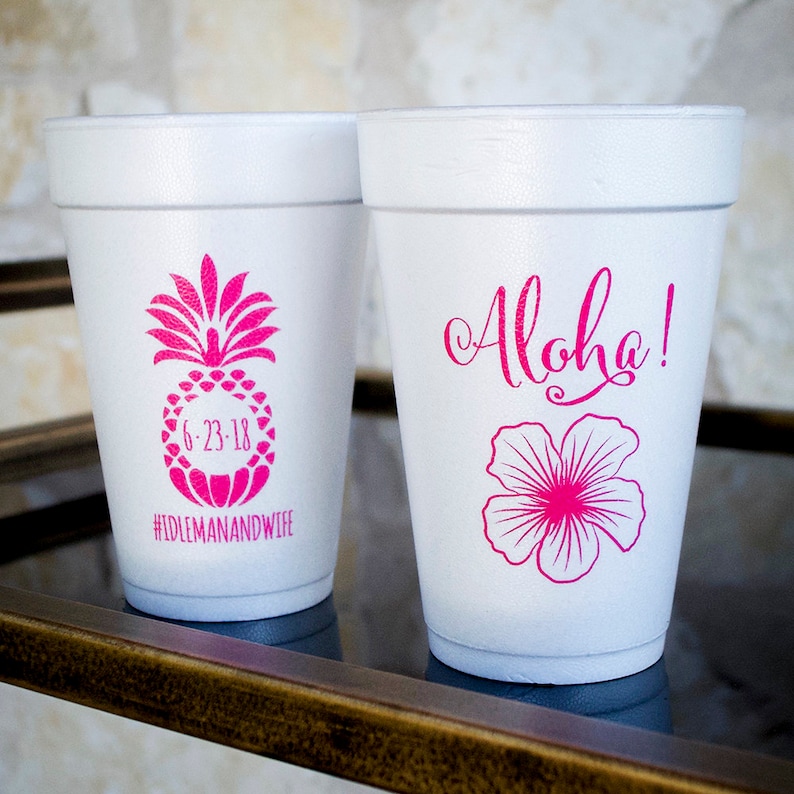 May include: Two white foam cups with pink designs. One cup has a pineapple with the text "6-23-18" and "#IDLEMANANDWIFE". The other cup has a pink hibiscus flower and the text "Aloha!"