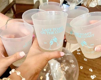 May include: A set of five translucent frosted plastic cups held in a group toast. Each cup features light blue text that reads LAST TOAST ON THE COAST, along with a graphic of two clinking champagne flutes and the year 2023 printed on them.