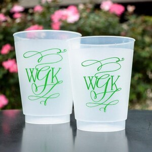 Könnte beinhalten: Zwei mattierte, durchscheinende Kunststoffbecher mit einem grünen Monogramm-Aufdruck der Buchstaben WGK in einer dekorativen Schreibschrift. Die Becher haben eine glatte, matte Oberfläche und eine konische Zylinderform mit einem Rand.