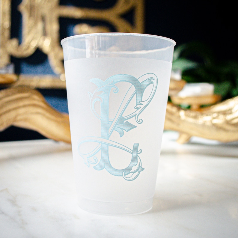 May include: A frosted plastic cup with a light blue monogram of the letter "L" in a decorative font.