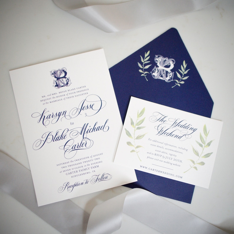 May include: A white wedding invitation with blue calligraphy announcing the marriage of Karsyn Jesse to Blake Michael Carter. The invitation includes the date, time, and location of the wedding ceremony and reception. A smaller card with a blue and green floral design invites guests to "The Wedding Weekend" and provides a website for additional information.