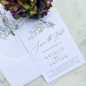 Könnte beinhalten: Save-the-Date-Karte mit einem Aquarell-Blumendesign in Blautönen und Grün. Der Text lautet "Save the Date" für die Hochzeit von Natalie und Patton. Das Datum ist Samstag, der vierzehnte Januar zweitausenddreiundzwanzig. Der Ort ist Austin, TX. Eine formelle Einladung folgt. Die Website ist www.natalieandpatton drewett.com.