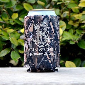 May include: A camouflage print beverage cooler sleeve featuring a large white decorative letter B monogram, with the text ERIN & CHRIS and the date JANUARY 24, 2015 printed in white below the monogram on the front of the cylindrical fabric holder.