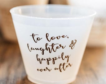 May include: A translucent white plastic cup featuring the brown printed text "to love, laughter & happily ever after" in a cursive script font. The cup has a wide, open top and a tapered base, with a smooth, matte finish throughout the exterior surface.