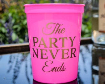 May include: A bright neon pink plastic stadium cup featuring the text The PARTY NEVER Ends printed in a bold gold font. The cup has a wide rim and a tapered cylindrical shape, with the text centered on the front surface of the vessel.