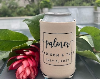 May include: A beige foam can cooler sleeve featuring a black rectangular border with the name "palmer" in script, followed by "MADISON & TRES" and the date "JULY 3, 2022" in a clean, sans-serif font, positioned next to a red ginger flower.