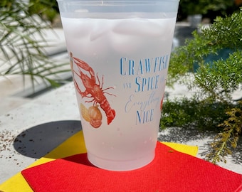 Könnte beinhalten: Ein durchscheinender Kunststoffbecher gefüllt mit Eis, verziert mit einer roten Flusskrebs-Illustration und dem blauen Text "CRAWFISH AND SPICE AND Everything Nice" auf der Seite. Der Becher steht auf einer leuchtend gelben und roten Serviette.