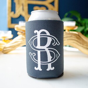 May include: A dark gray foam beverage insulator sleeve featuring a large, white, stylized monogram of the letters R and S intertwined in a decorative serif font. The sleeve is cylindrical and designed to fit snugly around a standard metal drink can.
