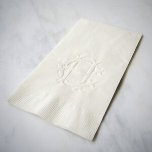 May include: A white linen napkin with an embossed monogram of the letter "H" in a decorative font.