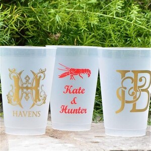May include: Three frosted plastic cups. The left cup features a gold letter H and the word HAVENS. The center cup displays a red crawfish graphic above the text Kate & Hunter. The right cup shows a gold monogram with the letters JB.