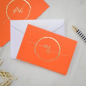 May include: Two orange envelopes with white envelopes inside. The envelopes have gold foil lettering with the initials "MW" and the name "Melony Woodard".