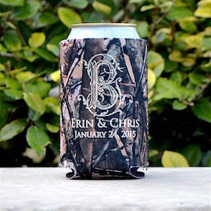 May include: A camouflage-patterned can cooler with the names "Erin & Chris" and the date "January 24, 2015" printed in white. A large, ornate letter "B" is centered on the cooler. The cooler is designed to insulate a standard-sized beverage can.