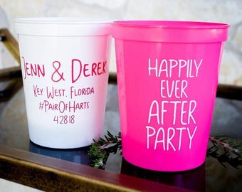 May include: A white plastic cup with pink text reading Jenn & Derek, Key West, Florida, #PairOfHarts, 4.28.18 and a hot pink plastic cup with white text reading Happily Ever After Party. Both cups have a smooth finish and a wide rim.