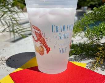 Puede incluir: Un vaso de plástico transparente esmerilado con un diseño de cangrejo de río y el texto "Crawfish and Spice and Everything Nice". El vaso está sobre una servilleta roja y amarilla.
