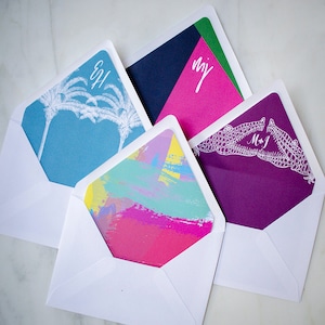 May include: Four white envelopes with different colored inserts. The inserts feature a palm tree design, abstract brushstrokes, a crocodile design, and a geometric design. The envelopes are blank except for the initials "GH", "MJ", and "NY" written in white.