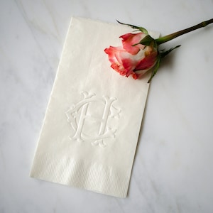 May include: White linen napkin with an embossed monogram of the letter "H" and a pink rose on top.
