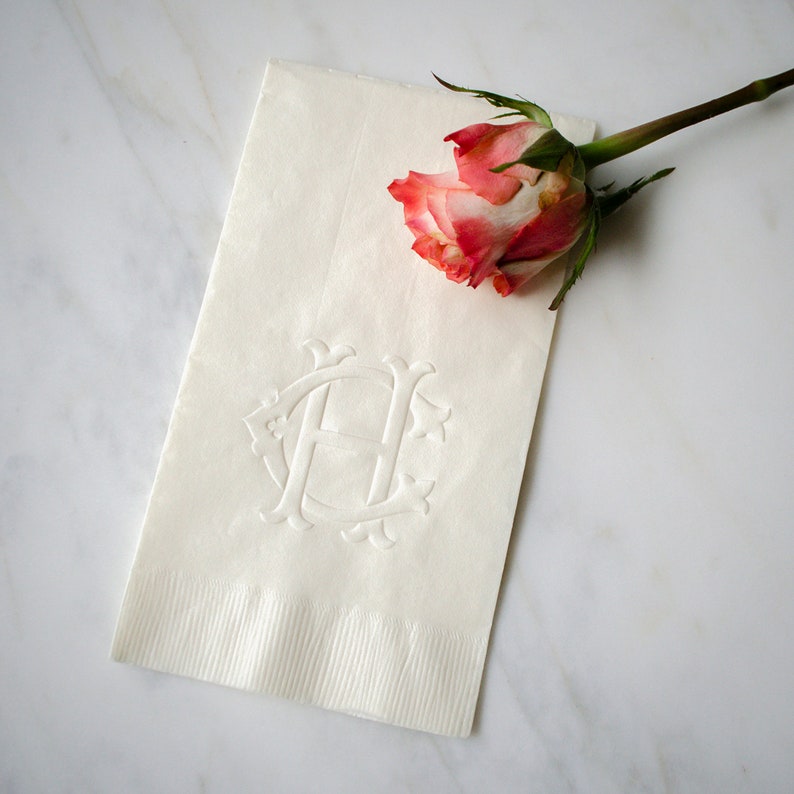 May include: White linen napkin with an embossed monogram of the letter "H" and a pink rose on top.