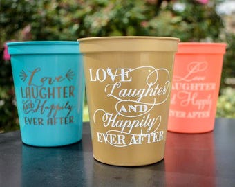 May include: Three plastic stadium cups in turquoise, gold, and coral. Each cup features the white text "LOVE Laughter AND Happily EVER AFTER" printed on the front. The cups have a tapered cylindrical shape with a wide rim and a smooth finish.