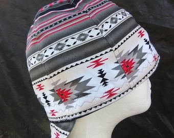 May include: A patterned welding cap in shades of gray, red, and white, displayed on a mannequin head. The cap features a geometric design with stripes and diamond shapes, offering protection and style.