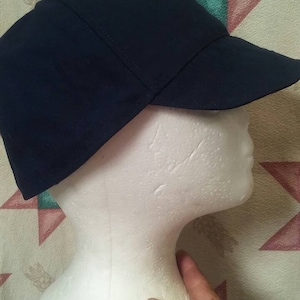 May include: A dark blue, cotton, work cap with a stiff brim. The cap is on a white styrofoam head.