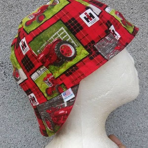 May include: Red and green fabric hat with a plaid pattern and a repeated image of a red tractor with the text "International Harvester" and "Farmall". The hat has a label that says "Made in USA".