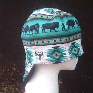 May include: A turquoise, white, and brown welding cap with a geometric pattern and a silhouette of a buffalo. The cap has a flap that can be worn down or up.