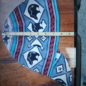 Puede incluir: Una gorra de soldadura estampada con un dise&ntilde;o nativo americano. La gorra presenta un patr&oacute;n repetido de siluetas de osos negros, diamantes y huellas de patas sobre un fondo gris. La gorra mide aproximadamente 20 cm de largo.
