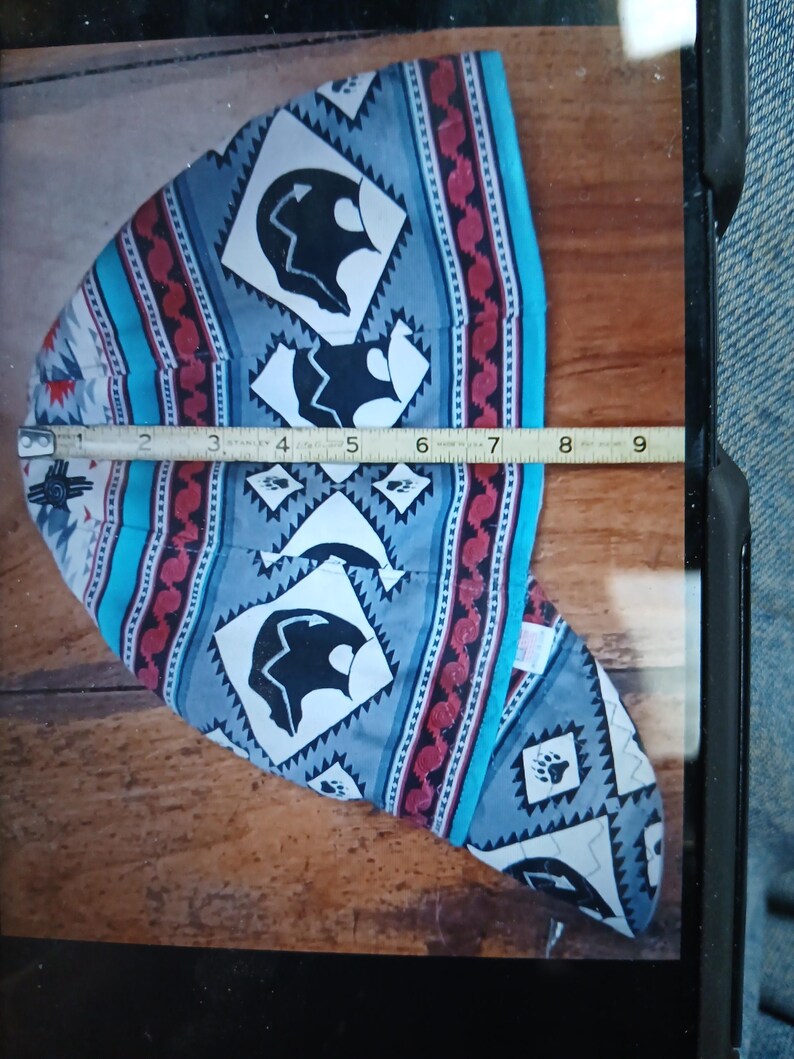 Puede incluir: Una gorra de soldadura estampada con un dise&ntilde;o nativo americano. La gorra presenta un patr&oacute;n repetido de siluetas de osos negros, diamantes y huellas de patas sobre un fondo gris. La gorra mide aproximadamente 20 cm de largo.