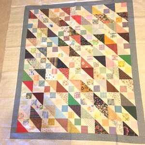 May include: A handmade quilt with a patchwork design. The quilt features a variety of fabric patterns and colors, including triangles and squares in shades of red, blue, green, and yellow. The quilt is bordered with a light blue fabric.