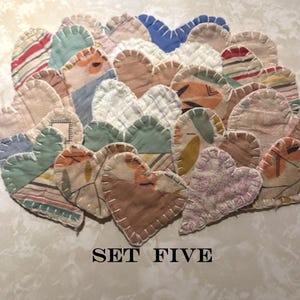 May include: A collection of heart-shaped fabric patches featuring various patterns and colors including blue, green, orange, and striped designs. Each heart is finished with visible white blanket stitching along the edges. The text SET FIVE is printed below.