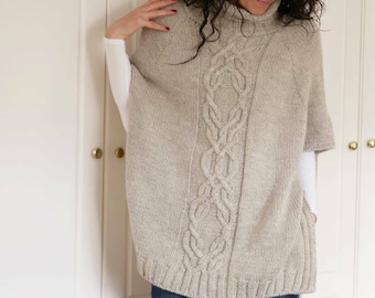 May include: A light grey knitted poncho with a cable knit pattern and a turtleneck collar.
