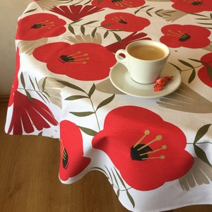 Può includere: Tovaglia bianca con un motivo floreale di papaveri rossi. Una tazza di caffè e un dolce sono su un piattino bianco sulla tovaglia.