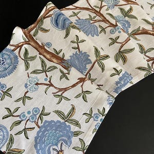 Puede incluir: Un camino de mesa de tela blanca con un patrón floral azul y marrón. El patrón presenta flores y hojas estilizadas.