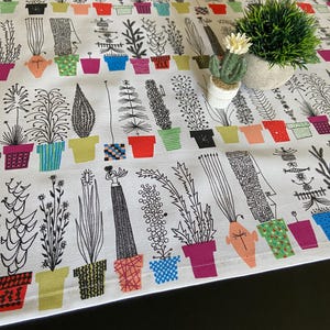 Puede incluir: Un camino de mesa blanco con un patrón repetitivo de plantas en maceta en blanco y negro con macetas de colores. Las plantas están estilizadas y tienen diferentes formas y tamaños. El camino de mesa es perfecto para agregar un toque de fantasía a cualquier mesa.