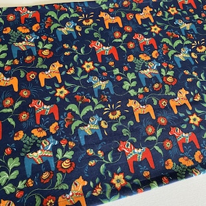 Könnte beinhalten: Ein marineblauer Stoff mit einem sich wiederholenden Muster aus bunten schwedischen Dala-Pferden und floralen Designs. Die Pferde sind in Rot-, Orange-, Gelb-, Blau- und Grüntönen bemalt.