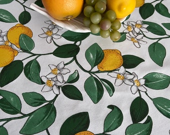 Puede incluir: Mantel blanco con un patrón de árbol de limón. El mantel presenta hojas verdes, flores blancas y limones amarillos. Un tazón blanco con una toronja, uvas verdes y limones está sobre el mantel.