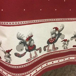 Peut inclure: Nappe de Noël rouge et blanche avec une bordure de motifs géométriques blancs et gris. La nappe présente un motif répété de rennes et de lutins portant des chaussettes rayées rouges et blanches.
