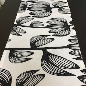 Puede incluir: Un camino de mesa blanco y negro con un patrón floral. El diseño presenta flores estilizadas con un patrón repetitivo.