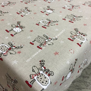 Könnte beinhalten: Beige Weihnachtstischdecke mit einem sich wiederholenden Muster aus skurrilen Rentieren mit roten Akzenten. Die Rentiere tragen Schals und haben dekorative Geweihe. Schneeflocken sind über dem Stoff verstreut. Die Tischdecke besteht aus einem strukturierten Material.