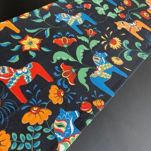 May include: Black table runner with a repeating pattern of colorful Swedish Dala horses, flowers, and leaves.