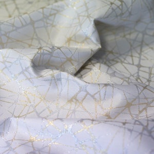 May include: White fabric with a geometric pattern of gold and silver lines. The fabric is textured and has a subtle sheen.