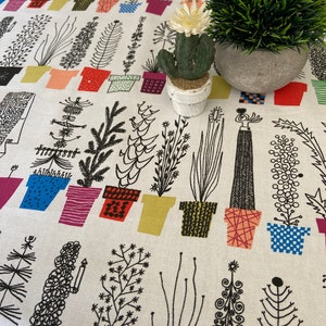 Può includere: Tessuto bianco con un motivo ripetitivo in bianco e nero di piante in vaso. Il tessuto presenta una varietà di forme e dimensioni di piante, tra cui cactus, felci e piante grasse. Un piccolo cactus in vaso con un fiore bianco si trova sopra il tessuto, insieme a una piccola pianta verde in vaso.