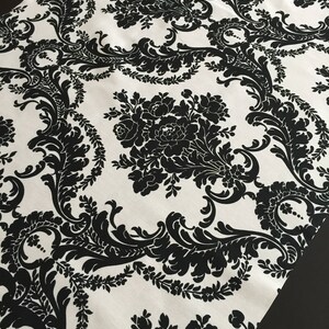 Puede incluir: Tela damasco en blanco y negro con un patrón floral. La tela tiene un fondo blanco con diseños florales negros.