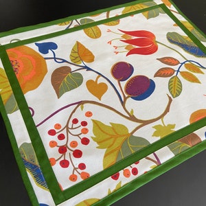 Peut inclure: Un set de table blanc avec une bordure verte et un motif floral composé de fleurs et de feuilles rouges, orange, jaunes, vertes, bleues et violettes.