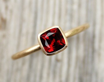 Può includere: Un anello d'oro con una pietra rossa di forma quadrata.