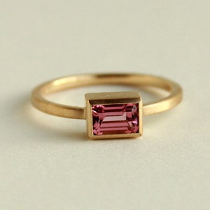 May include: A gold ring with a pink rectangular gemstone set in a gold bezel.