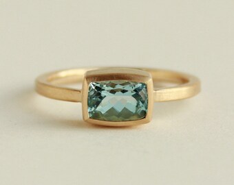 May include: A gold ring with a light blue aquamarine gemstone set in a square bezel.