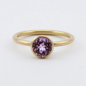May include: A gold ring with a bezel set purple gemstone.